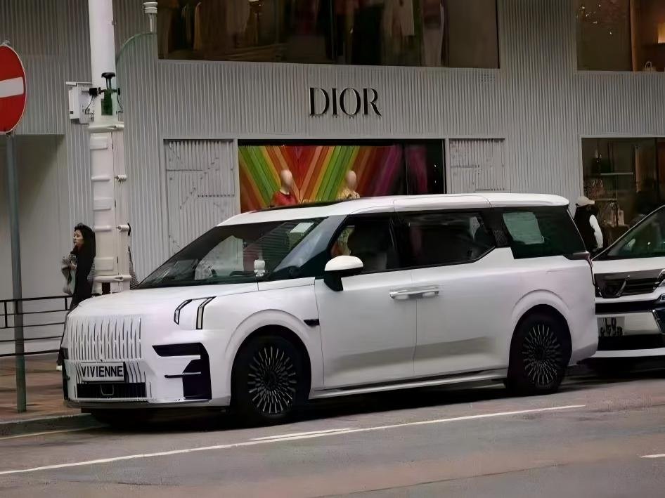 A sleek, white Zeekr 009 electric MPV parked on a cosmopolitan Hong Kong street directly in front of a luxury Dior boutique. The vehicle’s futuristic design and