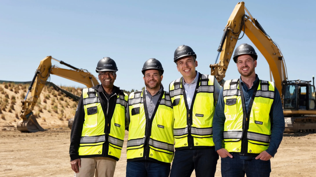 Bedrock Robotics team standing in front of autonomous excavators at a construction site