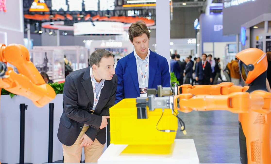 Visitors inspecting dual-arm industrial robots at a trade fair booth